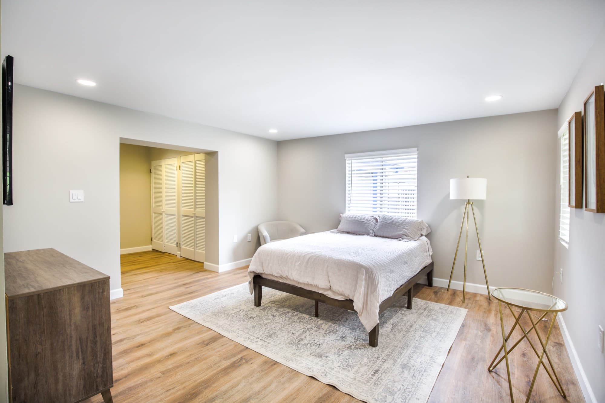 Master bedroom with queen bed, area rug, brass floor lamp, and walk-in closet