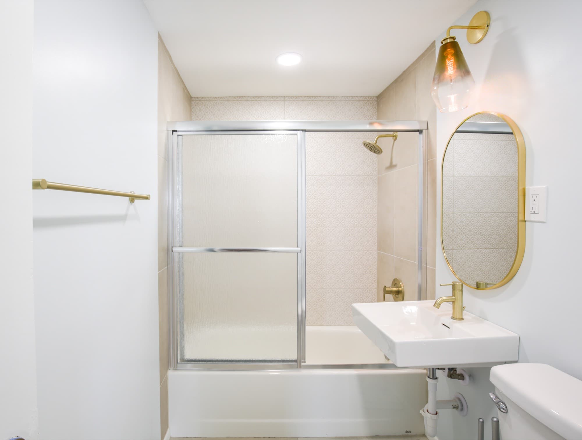 Bathroom with gold shower head, brass towel bar, and patterned tile surround