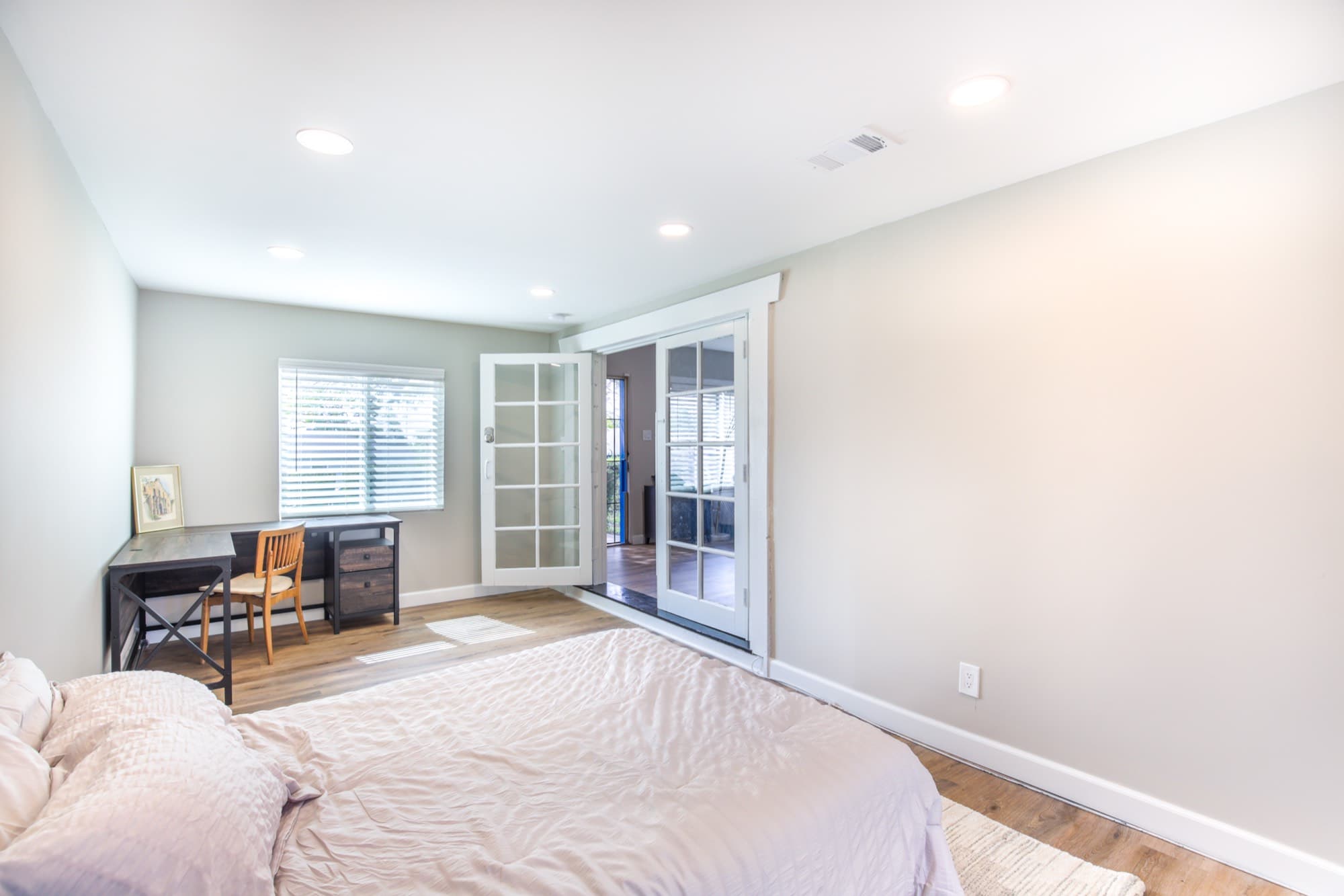 Bedroom with workspace desk, French doors to living area, and hardwood floors