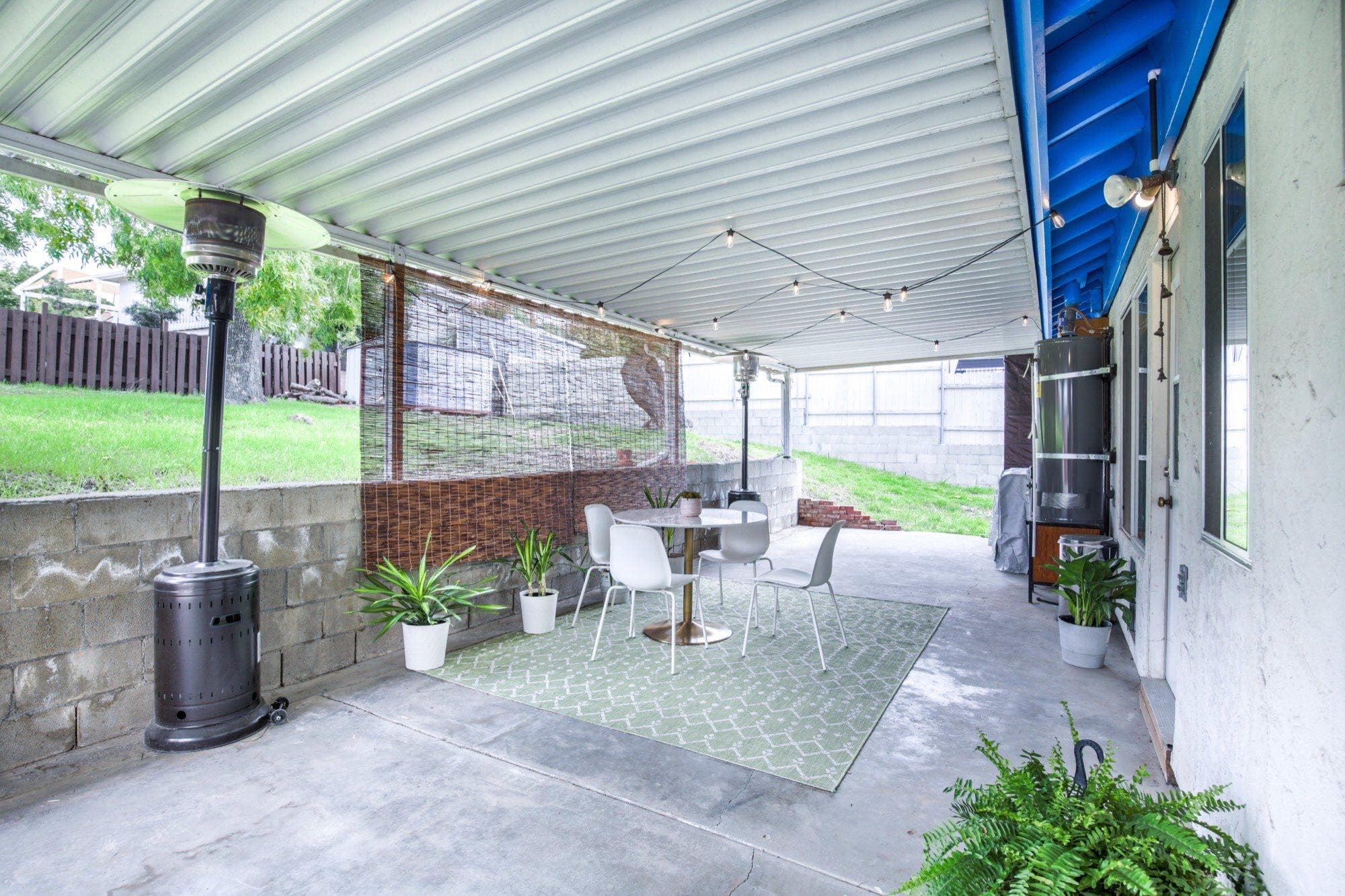 Covered patio with string lights, patio heater, dining set, and green backyard