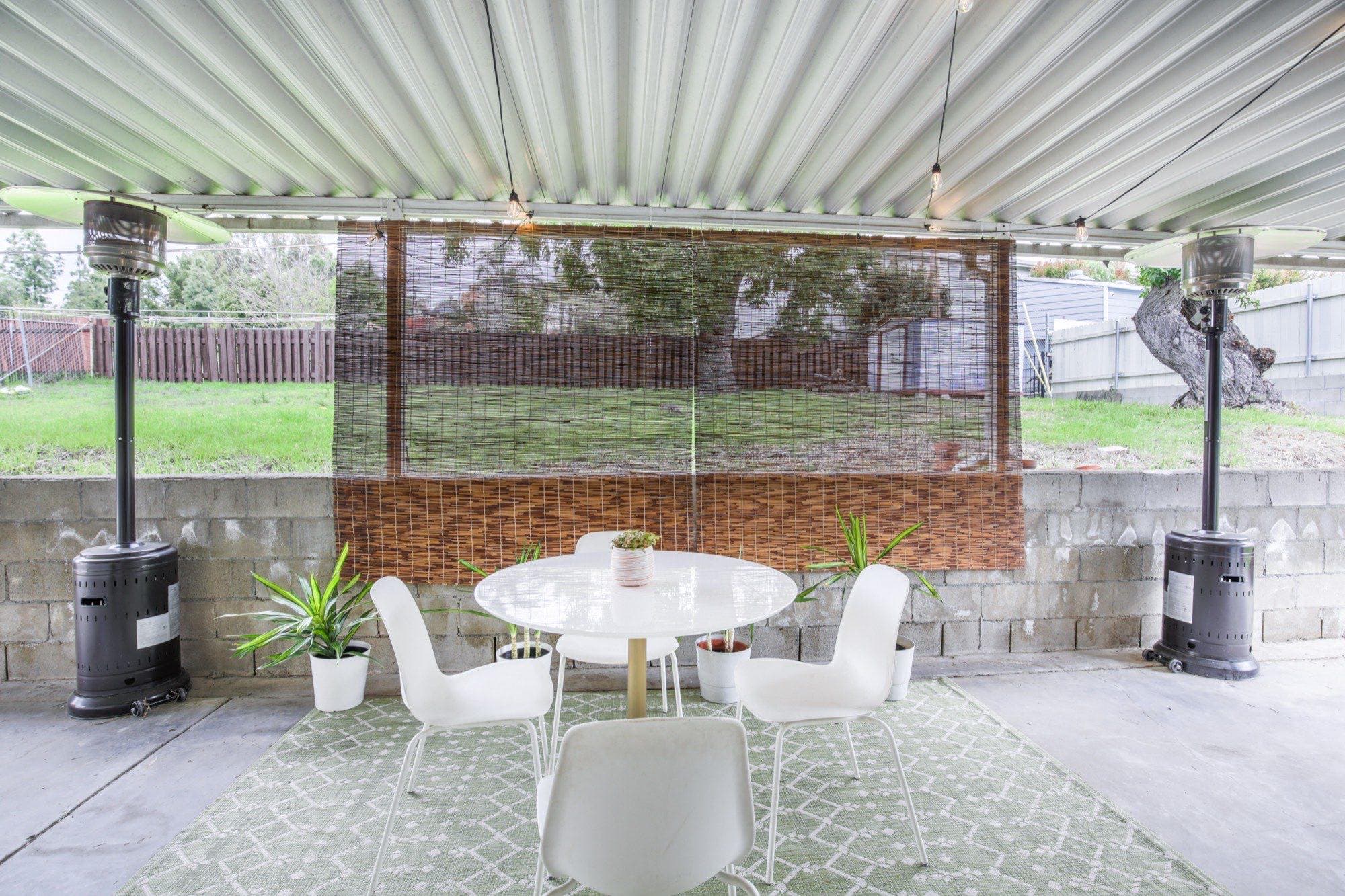 Covered patio dining area with modern chairs, dual heaters, and woven privacy screen